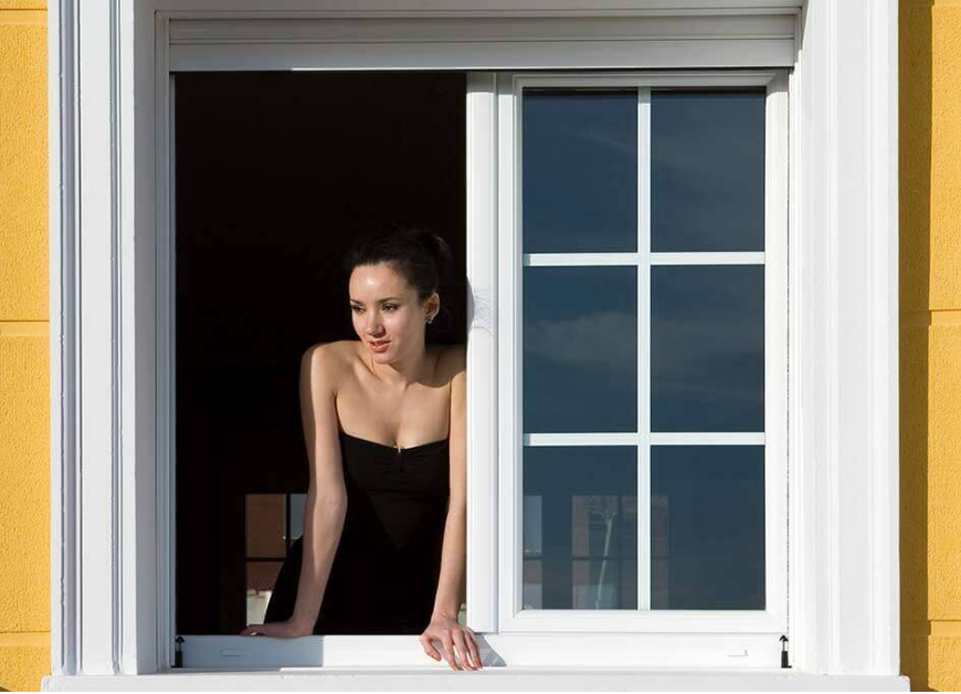 Mujer asomada en una ventana abatible Zendow de PVC blanco.